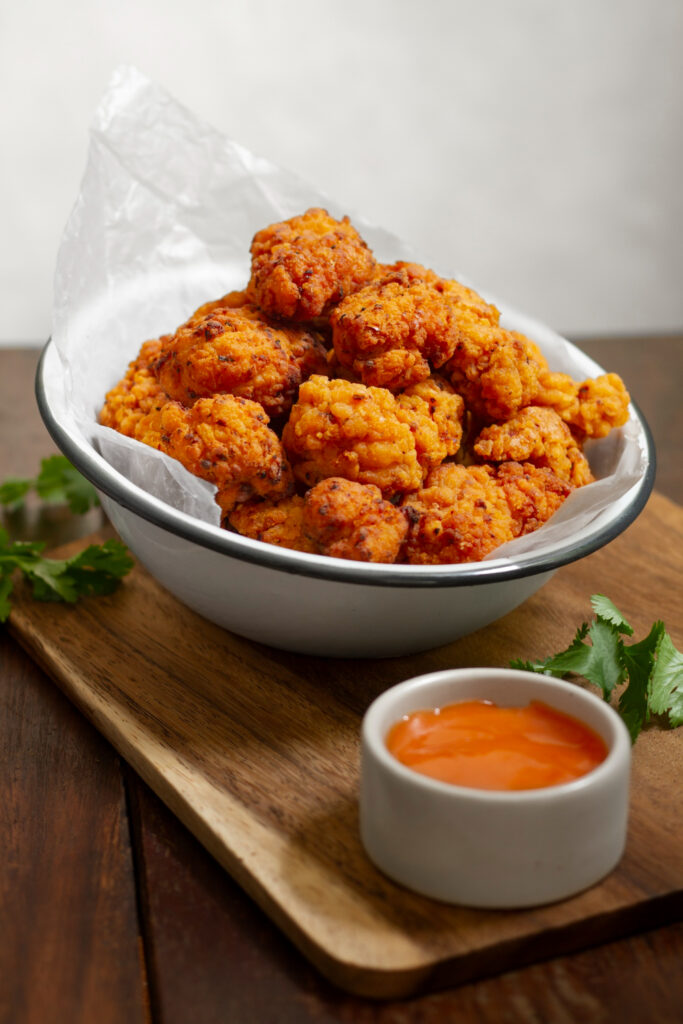 Air fryer basket with popcorn chicken midway through cooking, achieving golden crispiness